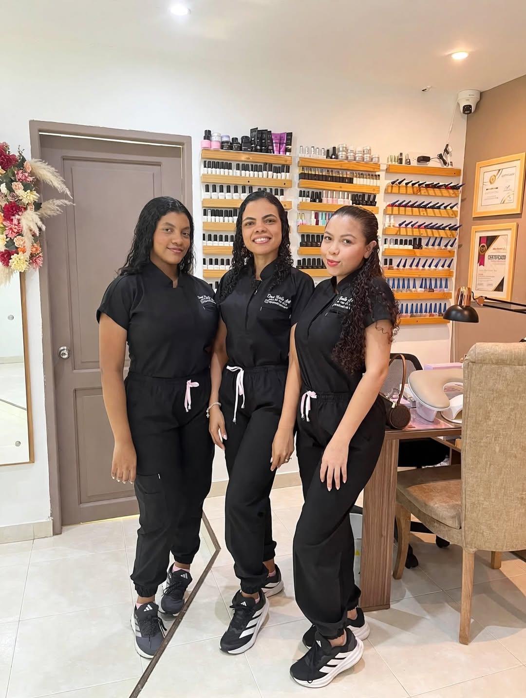 Desi y su equipo en el salón, de uniforme negro, frente a la pared de esmaltes